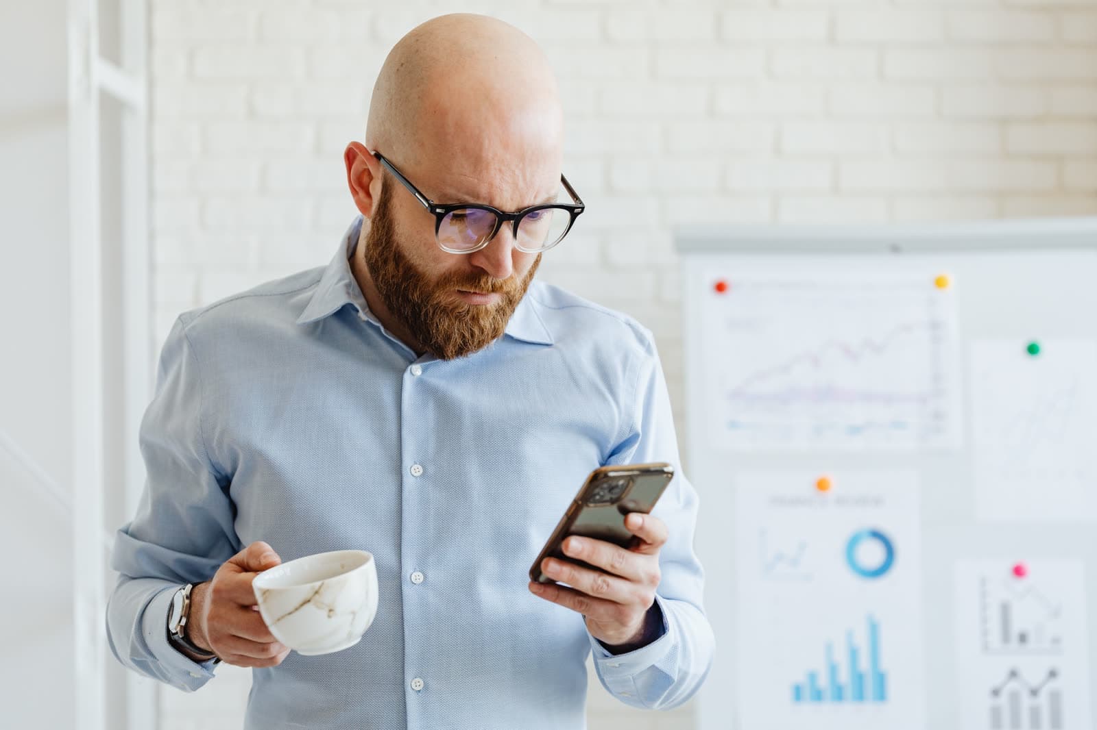 A sales manager checking the team's numbers on his phone, coffee in hand